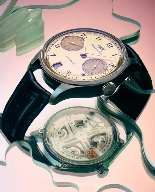IWC Schaffhausen watch with a black strap and a transparent case back, displayed on a glossy surface with ribbons, product photography.