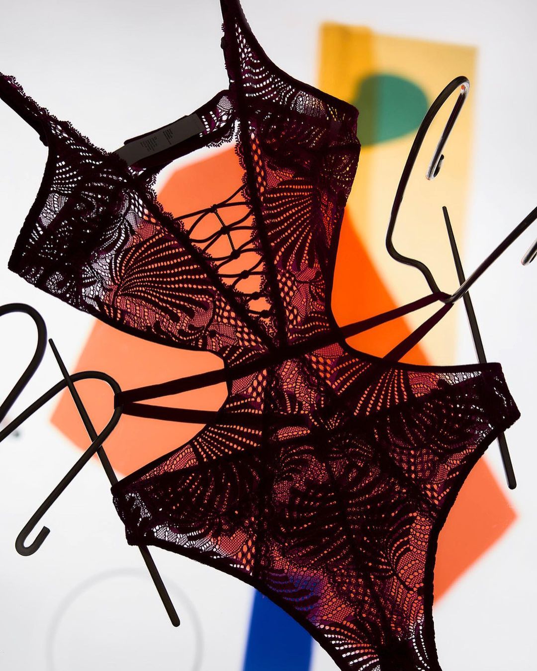 Elegant black lace lingerie showcased on a hanger with a geometric backdrop of orange and blue, fashionably displayed in a studio setting.