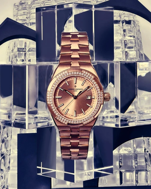 Luxury rose gold Vacheron Constantin watch featuring diamond bezel on clear crystal stands against a black and white background in a studio.