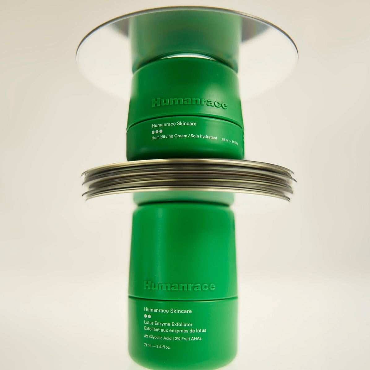Stacked green Humanrace skincare jars on mirrored surfaces, cosmetic product photography against a plain white background in studio lighting.
