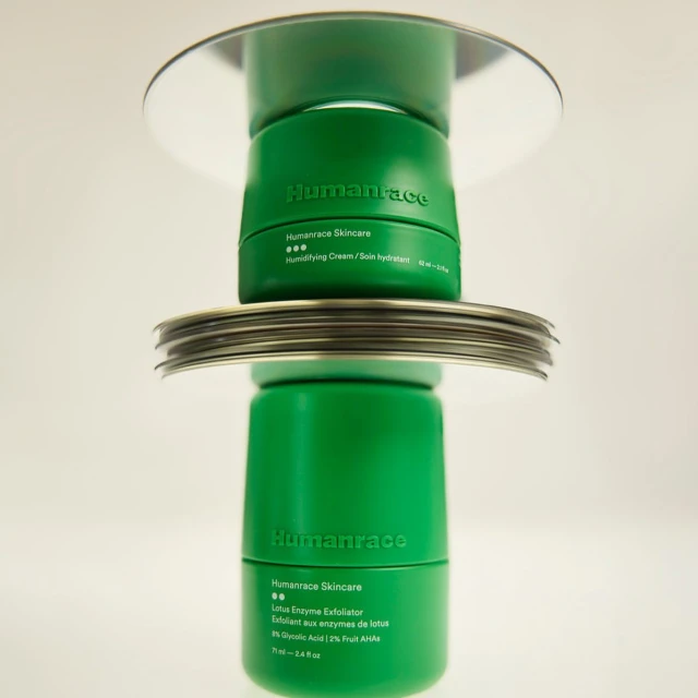 Stacked green Humanrace skincare jars on mirrored surfaces, cosmetic product photography against a plain white background in studio lighting.