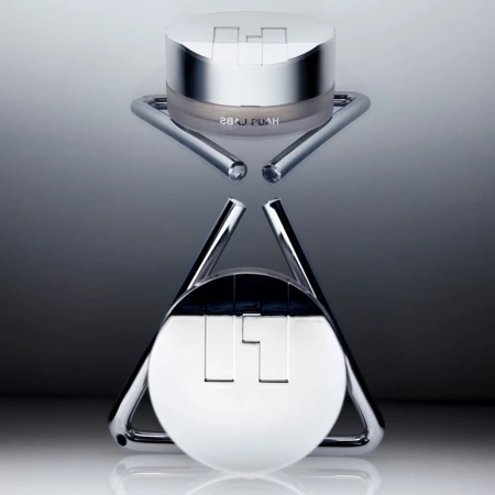 Cosmetic product shot of a Hyaluronic Acid moisturizing snow cushion compact sitting on a chrome display stand against a gradient background.