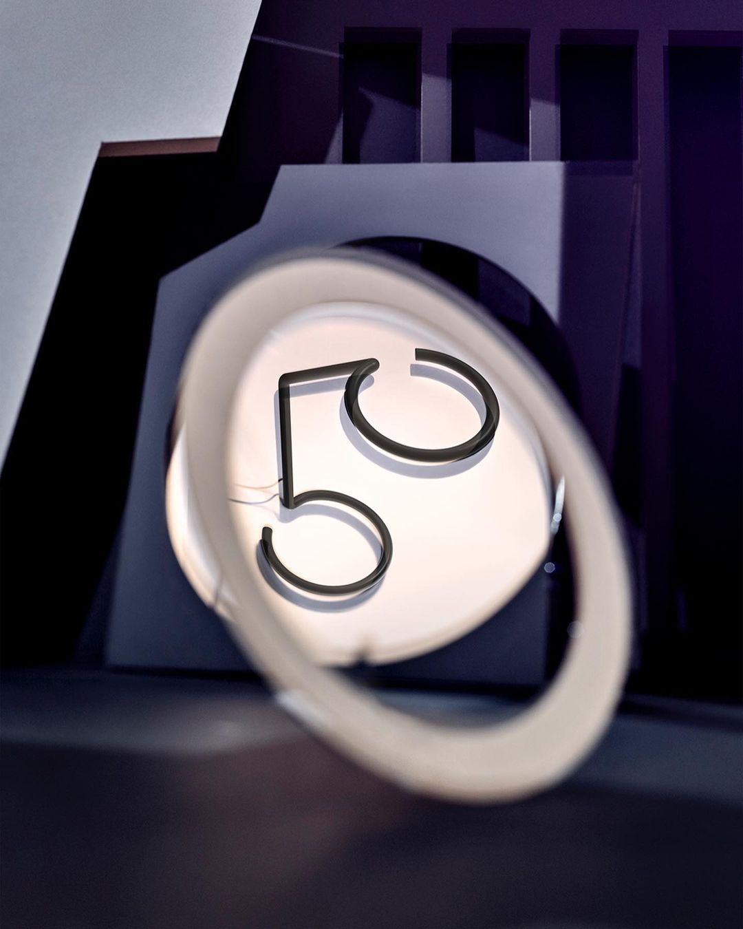 Close-up of an illuminated black number 5 inside of a white neon oval frame against a geometric, dark purple background.