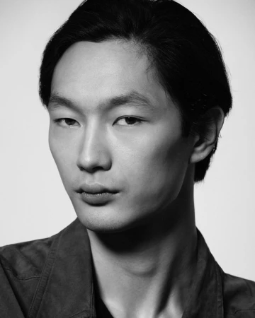 Close-up monochrome portrait of an East Asian man with dark hair against a plain light background by photographer Stratis Kas