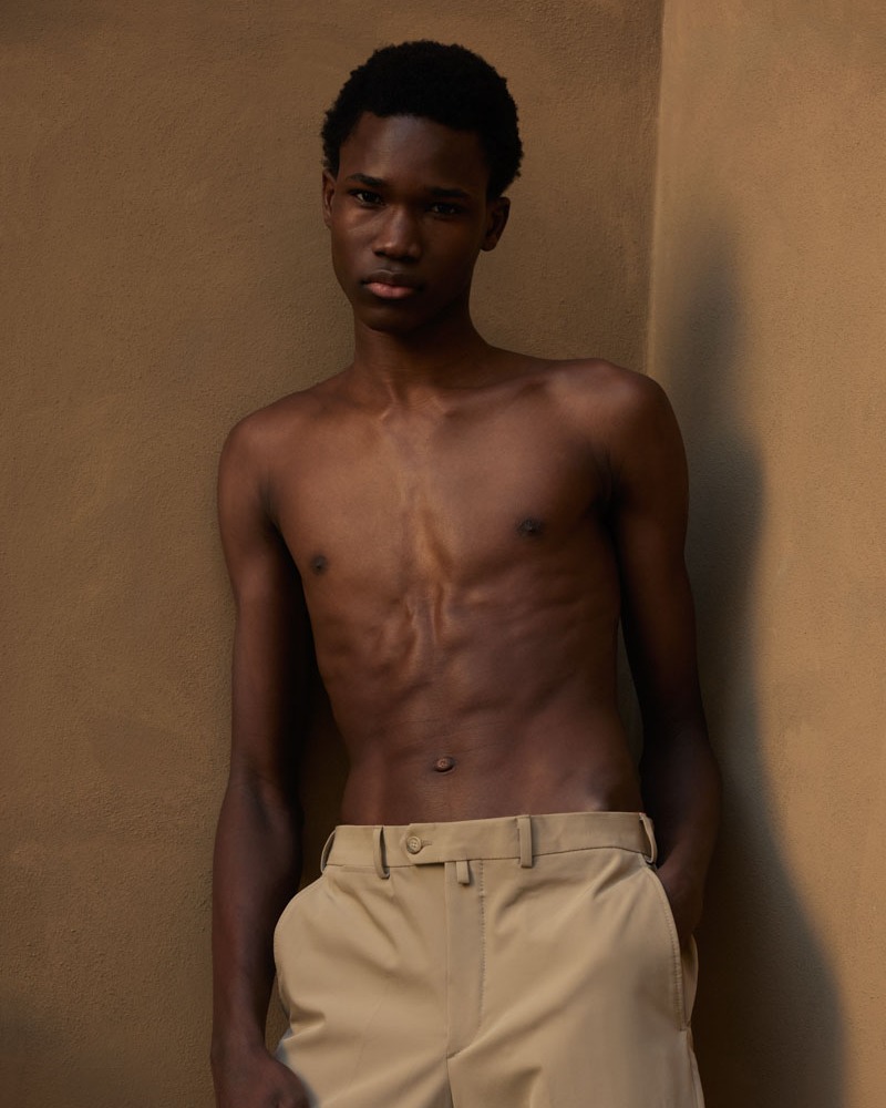 Portrait of a shirtless African-American man indoors against a neutral wall, wearing khaki pants and hands in pockets, casual fashion.