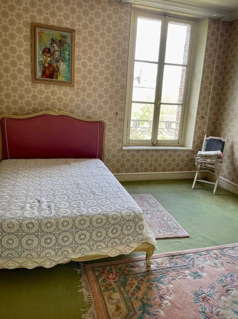 Bedroom interior featuring a red headboard bed with patterned cover, floral wallpaper, light green carpet, area rugs, and window.