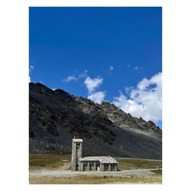Stone church at the base of a mountain under a blue sky with scattered clouds, rural environment, architectural photography.