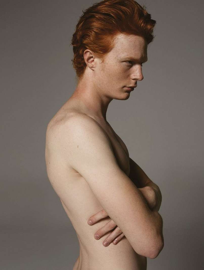 Profile portrait of a red-haired man with arms crossed against a plain grey studio backdrop