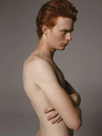 Profile portrait of a red-haired man with arms crossed against a plain grey studio backdrop