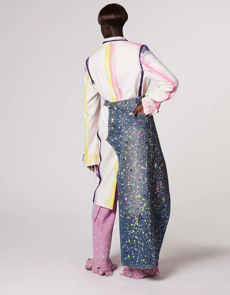 Fashion shot of a person in an abstract paint-splattered outfit.  The model faces away in a studio setting against a plain white backdrop.