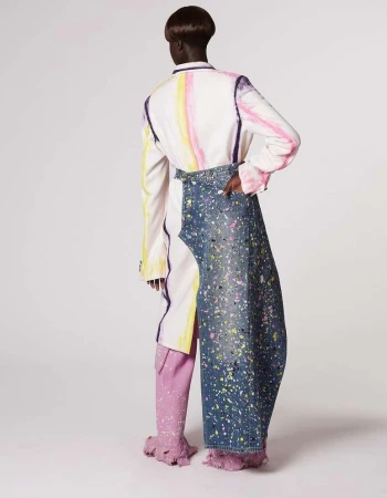 Fashion shot of a person in an abstract paint-splattered outfit.  The model faces away in a studio setting against a plain white backdrop.