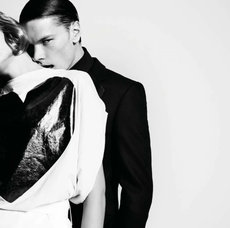 Close-up monochrome portrait of a man in a black jacket posing intimately behind a woman in a white top.