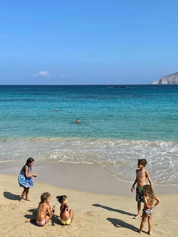 Group of children playing on a sandy beach with turquoise water and a clear blue sky in the background, creating a summery, playful scene.