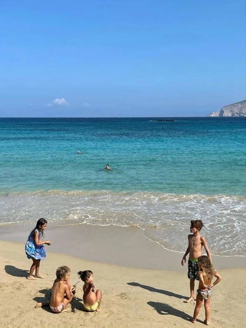 Group of children playing on a sandy beach with turquoise water and a clear blue sky in the background, creating a summery, playful scene.