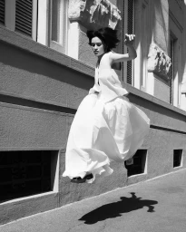 Model wearing a white dress jumping mid-air in front of a stone building exterior in Paris captured by Stratis Kas