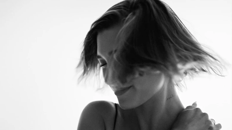 Close-up portrait of a woman with short dark hair flipping across her face against a bright background