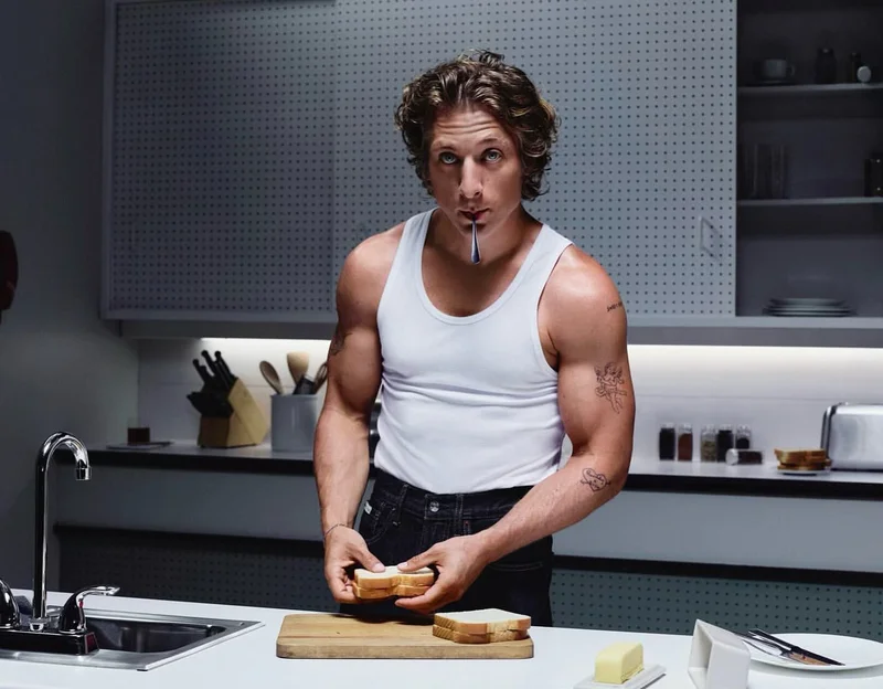 Jeremy Allen White in a white tank top assembling a sandwich in a commercial kitchen by photographer Stuart Winecoff