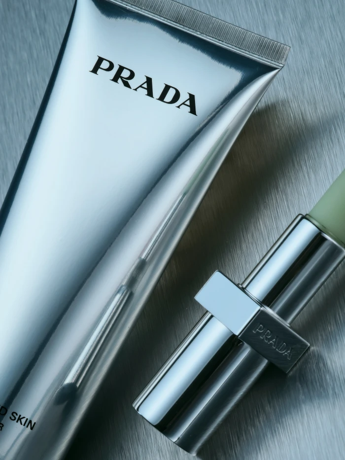 Prada beauty tube and lipstick product packaging on a vertical brushed metal background