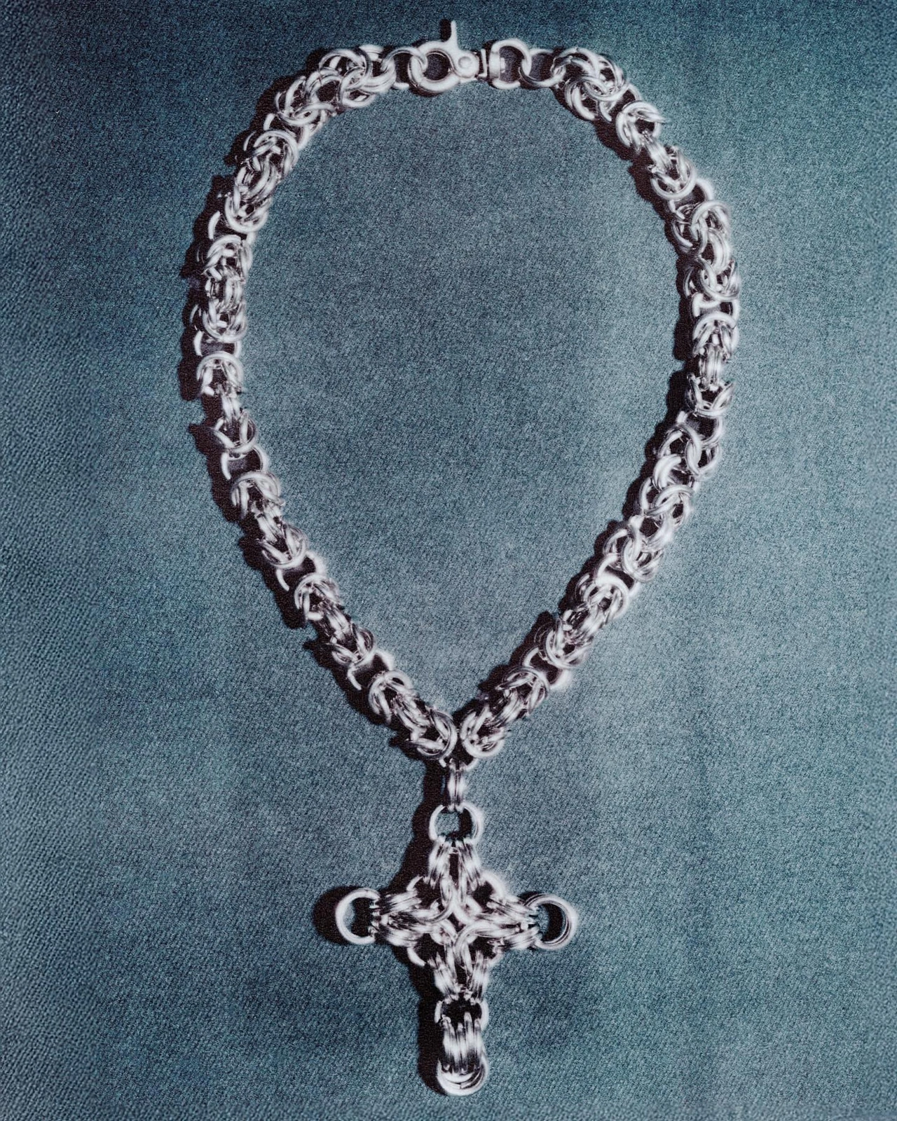 Silver chain necklace with an ornate cross pendant laid out flat against a dark textured background