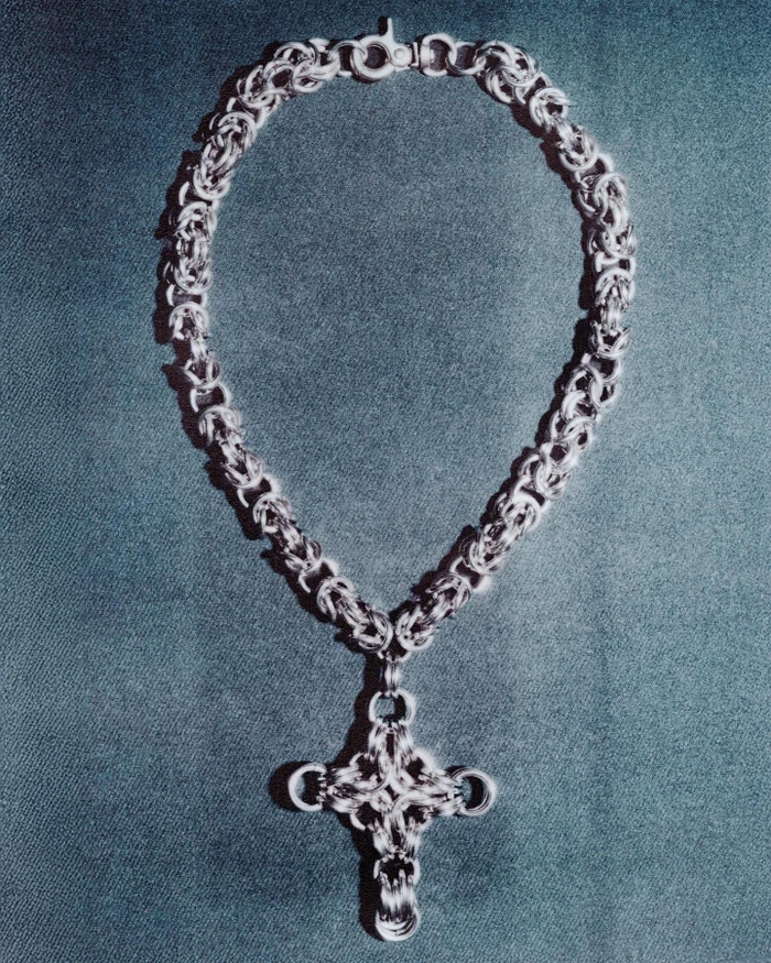 Silver chain necklace with an ornate cross pendant laid out flat against a dark textured background