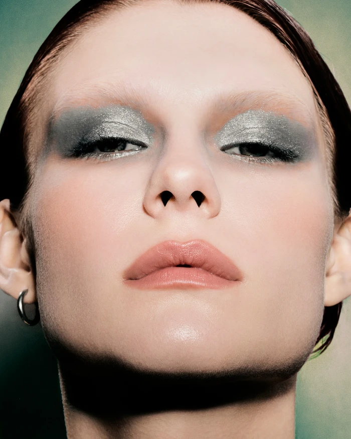 Close-up portrait of a woman with metallic silver eye shadow and natural pink lips by Caroline Pusset.