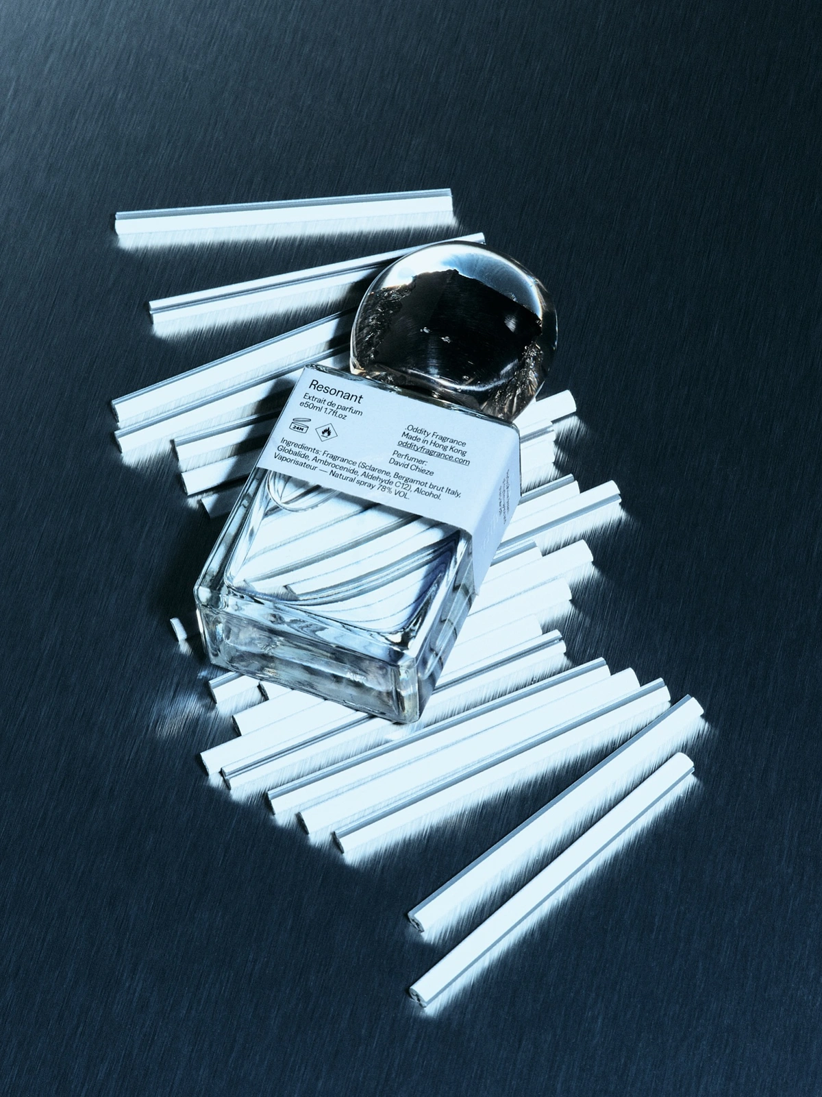 Resonant perfume bottle resting on a metallic brushed surface surrounded by numerous white tester strips