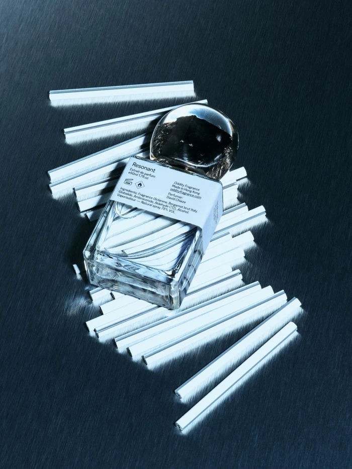 Resonant perfume bottle resting on a metallic brushed surface surrounded by numerous white tester strips