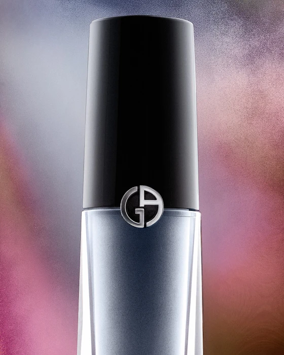 Close up product shot of a cylindrical cosmetic bottle with a black cap and silver logo against a soft abstract background