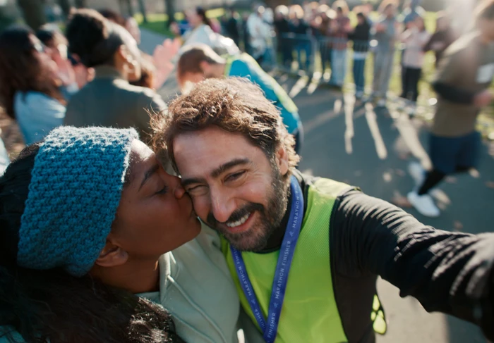 Woman kissing a smiling man wearing a running vest while taking a selfie