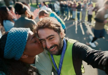 Woman kissing a smiling man wearing a running vest while taking a selfie