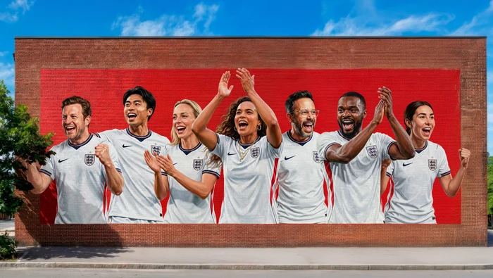 Seven people in white sports jerseys cheering and clapping in front of a large red brick wall mural