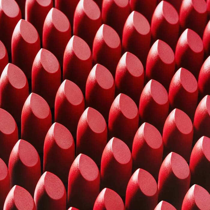 An array of red lipstick bullets arranged in a precise geometric grid pattern with sharp highlights.
