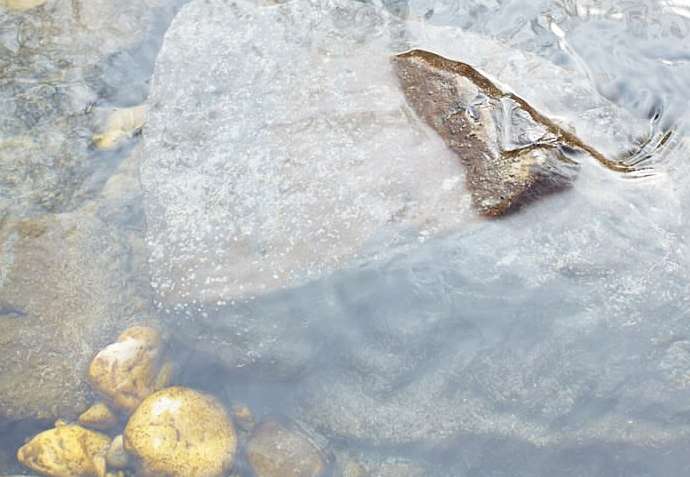 Rocks and water in a stream. Smooth rocks of different sizes are partially submerged by clear, moving water in a natural setting.