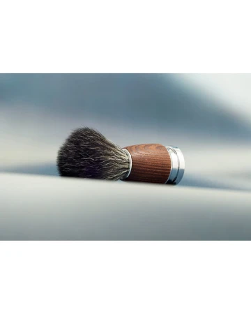 Close-up of a classic shaving brush with a dark wood handle and silver accents against a soft, gray background. Beauty and grooming.