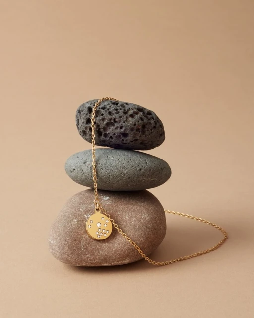Gold pendant necklace displayed on stacked stones against a beige background, minimalist jewellery still life, product shot.