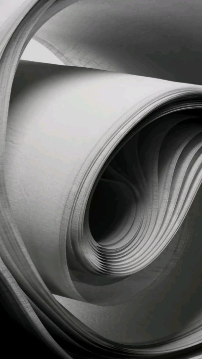 Monochromatic photograph of layered, swirling sheets of white paper creating a dynamic and abstract visual composition.