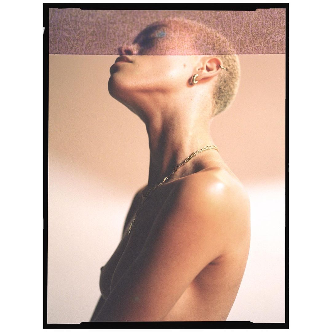 Close-up studio shot of a fair-skinned adult woman gazing upward, accentuated by natural light, gold jewelry, and bleached short hair.