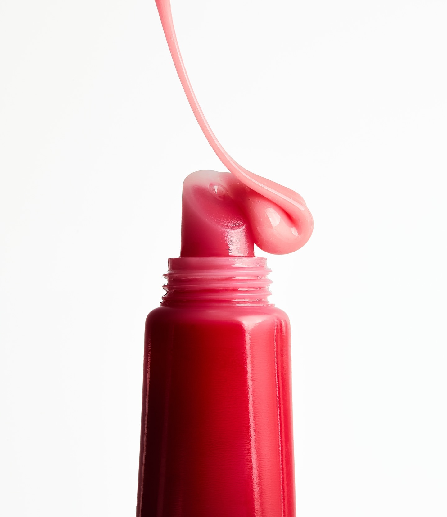 Close-up shot of a tube of lip gloss with a stream of pink liquid coming out, set against a clean white backdrop. Beauty product.