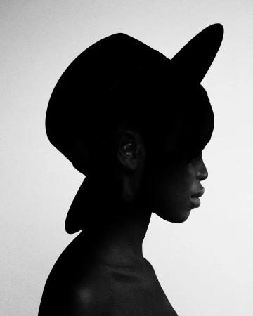 High contrast silhouette profile portrait of a woman wearing a wide-brimmed hat against a bright background.