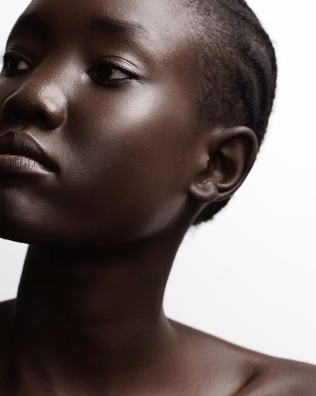 Close-up portrait of a Black female with dark skin and shaved hair, showcasing beauty and texture against a neutral backdrop.