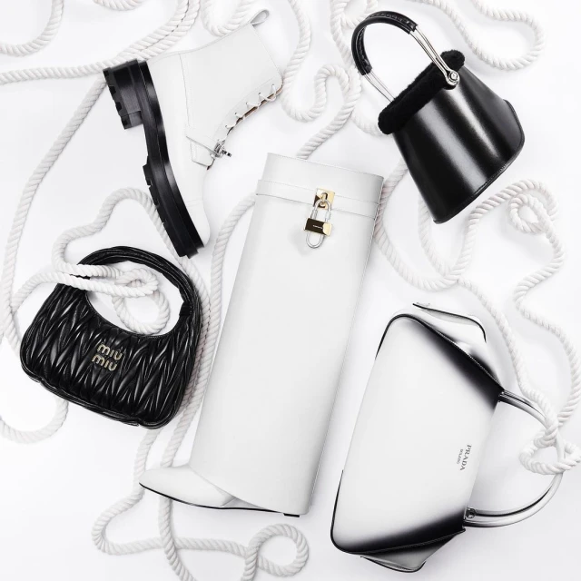 Elevated studio shot of luxury black and white designer handbags and boots arranged on a clean white background with white rope.