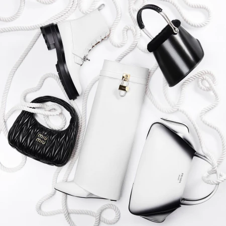 Elevated studio shot of luxury black and white designer handbags and boots arranged on a clean white background with white rope.