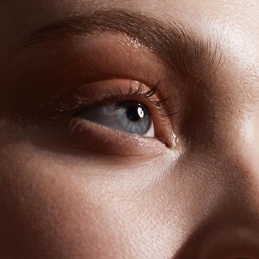 Close-up shot of a human face highlighting a blue eye with visible eyelashes and eyebrow, illuminated by bright lighting.