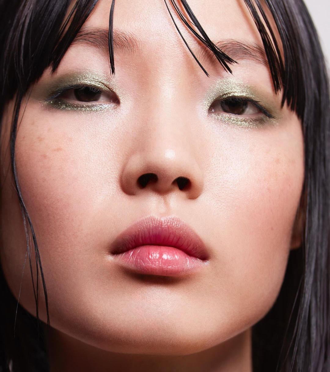 Close-up of an Asian adult female with green eyeshadow, black hair, and pink lips. Beauty shot for makeup and cosmetics.