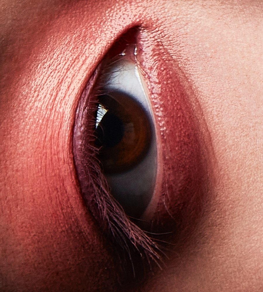 Macro shot of a human eye with visible eyelashes and skin texture, featuring a red color grading for a dramatic effect.