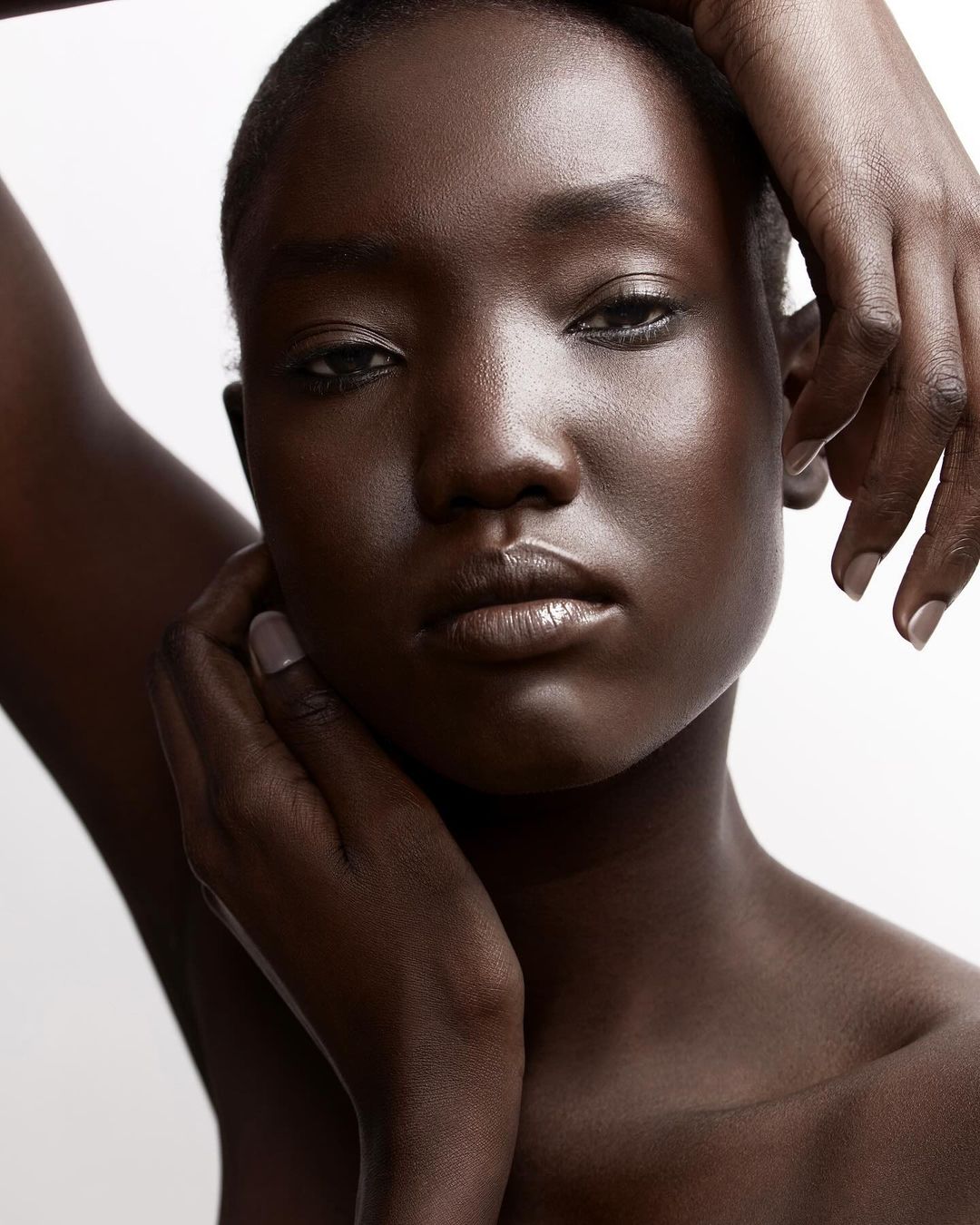 Close-up beauty portrait of a Black woman with hands framing her face against a white background