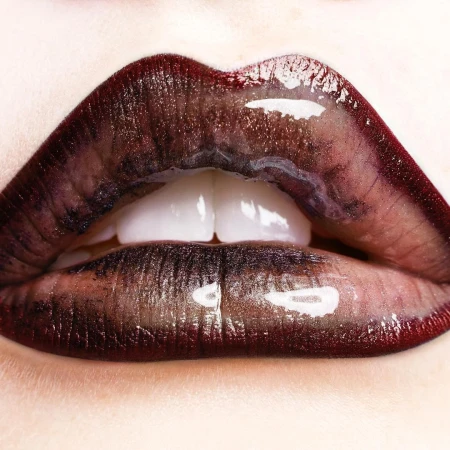 Macro close-up of human lips with glossy, dark red lipstick. The glossy texture highlights the lip's form and the teeth are partially visible.