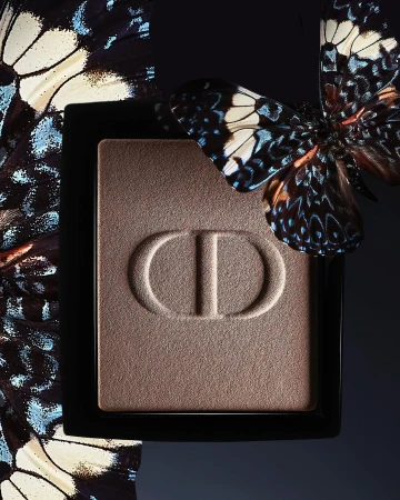 Close-up of Dior eyeshadow palette with CD logo, adorned with butterfly. Studio shot showcases beauty product with natural elements.