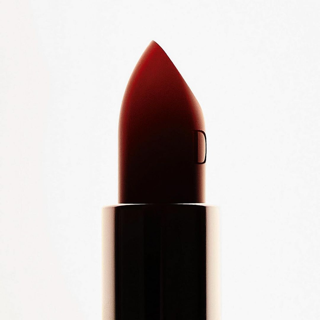 Close-up macro shot of a dark red lipstick bullet against a bright white seamless background