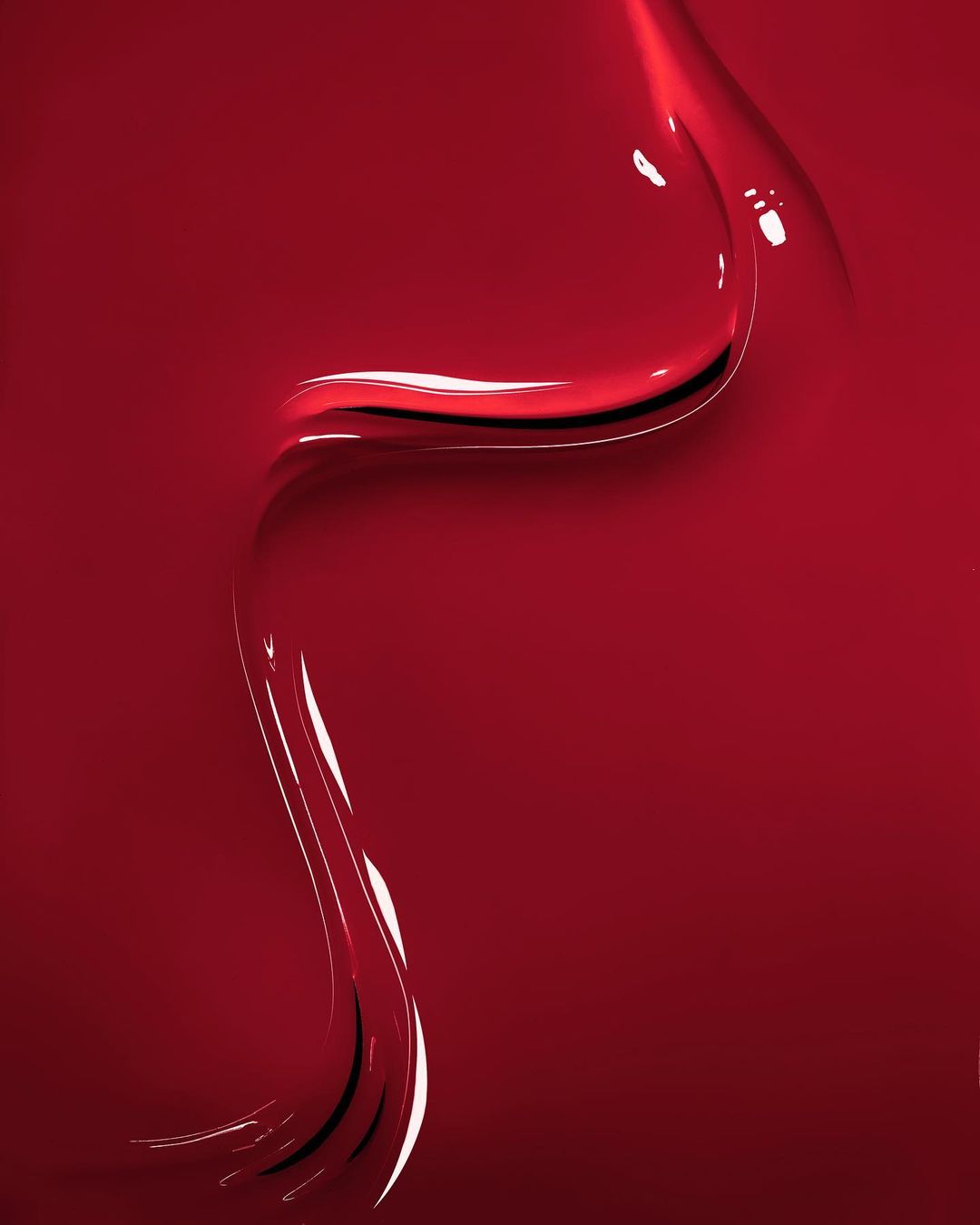 Abstract close-up of shiny, textured red fluid, possibly nail polish or paint, featuring glossy highlights and dark shadows.